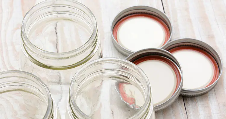 Closeup of three glass canning jars on a rustic wood farmhouse style kitchen table
