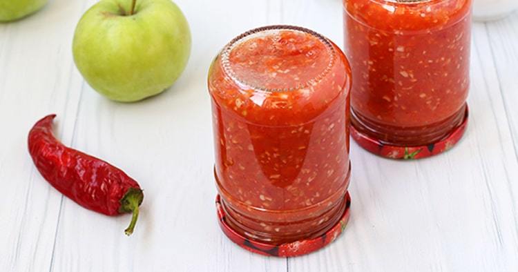 Adzhika with apples in jars on the table. Harvesting for the winter. The banks are turned upside down.