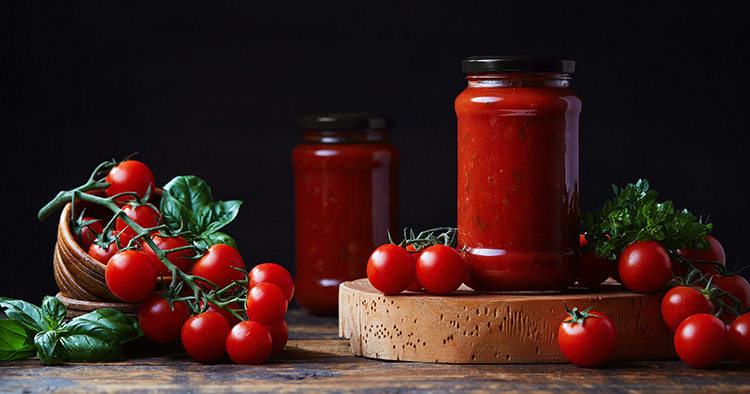 Homemade tomato sauce in a glass jar, tomatoes and herbs on its side