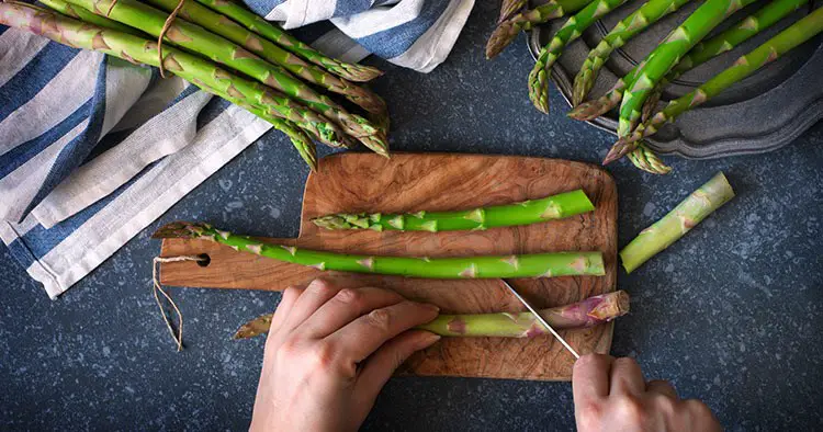 Women female hands cut asparagus on wooden cooking board