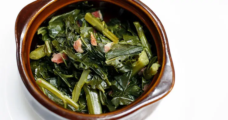 Gourmet homemade collard greens with pieces of ham in a bowl with a white background