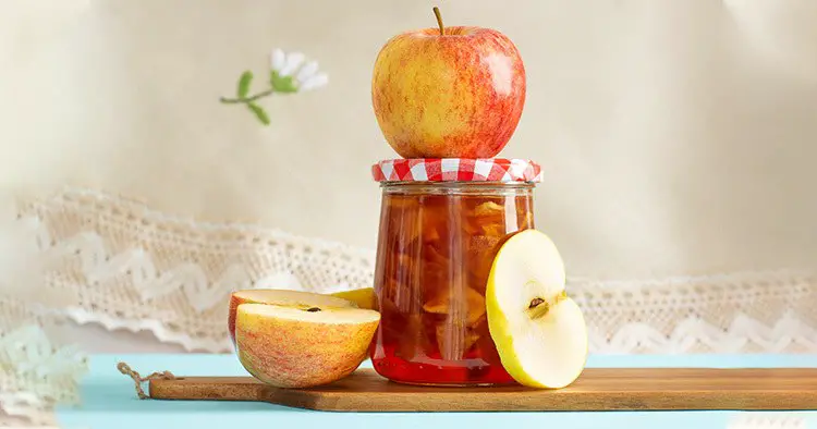 Glass jar of homemade apple jam and apples on kitchen board