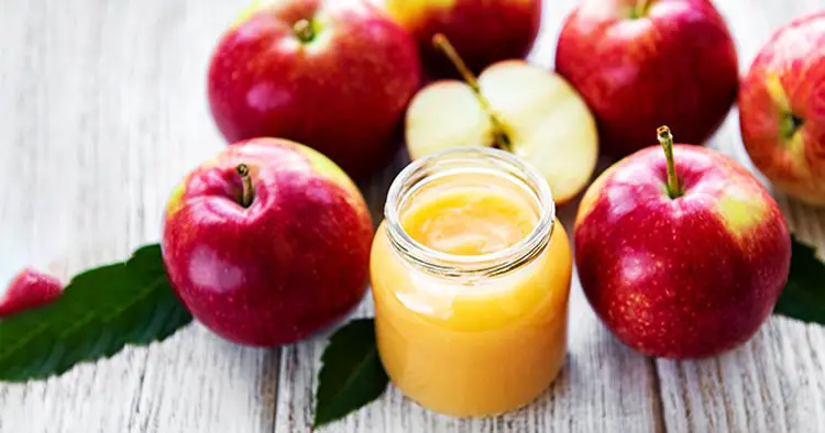 Applesauce in glass jar and fresh apples on a wooden table