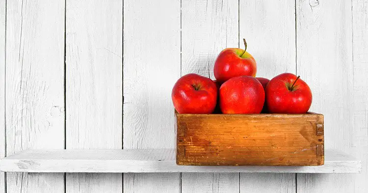 Apples in a box on a wooden shelf.