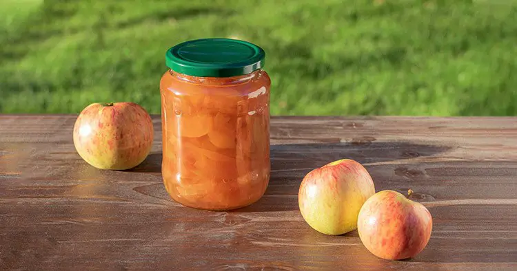 Glass jar with apple preserve on the wooden table among red and yellow apple fruits