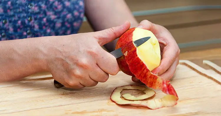 hands-peeling-cooking-apple-on-wooden