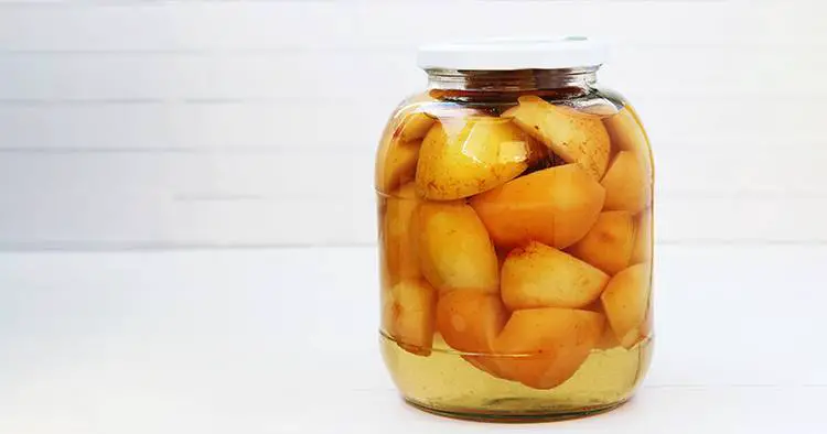 Canned apples in syrup in a jar on a white background.