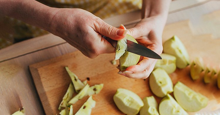 Charlotte apple pie baking - Woman in apron peeling apples and core - fruit filling