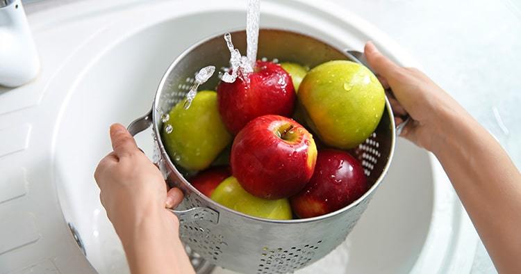 Young woman washing ripe apples in kitchen