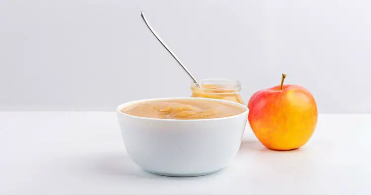 Fresh homemade applesauce in white bowl and jar with fruit puree on white table
