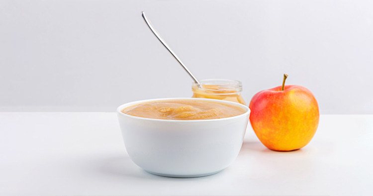 Fresh homemade applesauce in white bowl and jar with fruit puree on white table