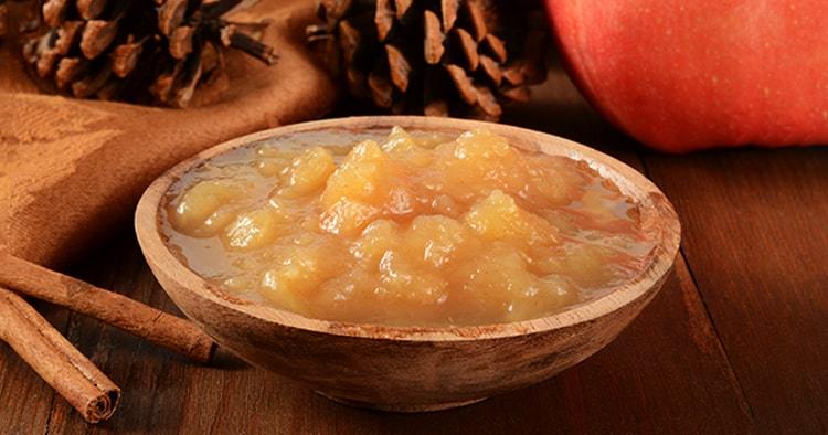 A wooden bowl of chunky applesauce with cinnamon sticks and pine cones