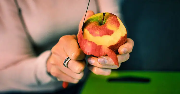 Close-up of hands peeling an apple. Woman's hands removes the skin of a red apple with a knife.