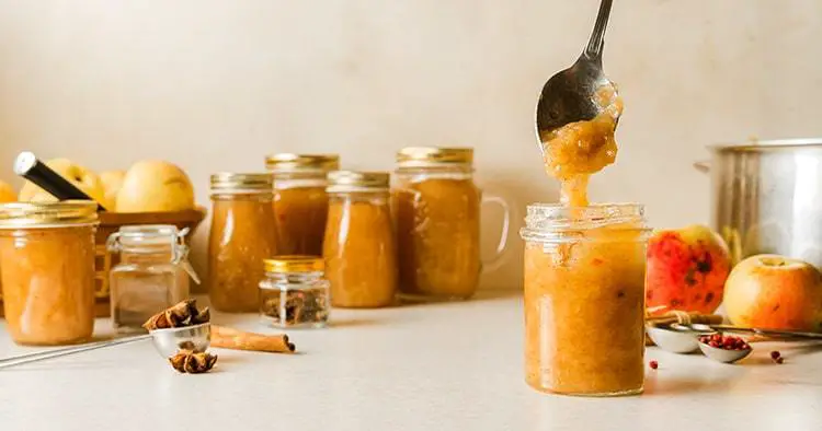 Woman spooning fresh homemade applesauce in glass jars on kitchen table. Vertical image with copy space