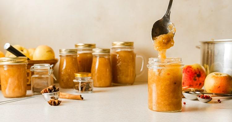 Woman spooning fresh homemade applesauce in glass jars on kitchen table. Vertical image with copy space