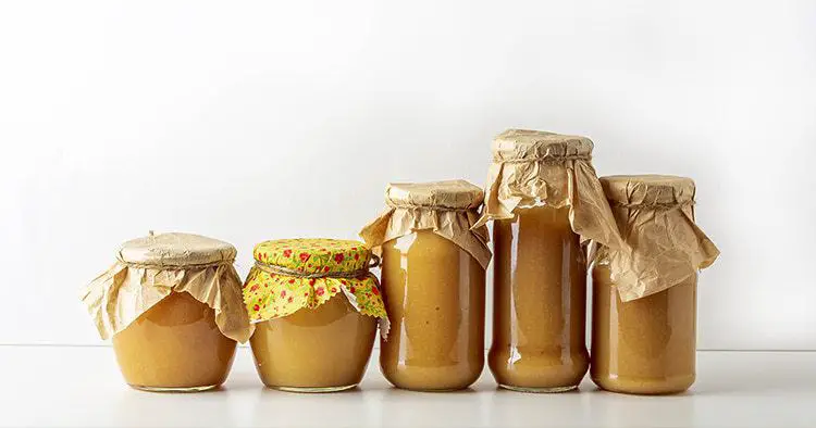 Canned and preserved applesauce in glass jars on white table