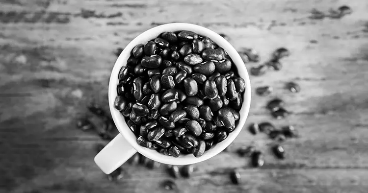 Raw black beans in basket and spoon on wood table.