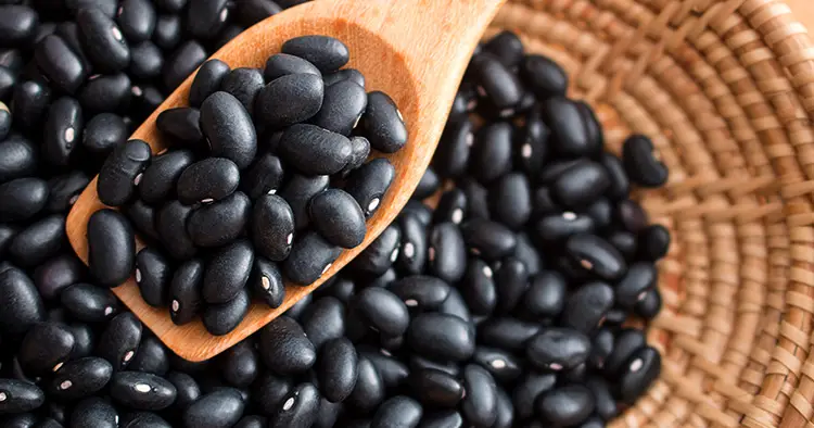 Raw black beans in basket and spoon on wood table.