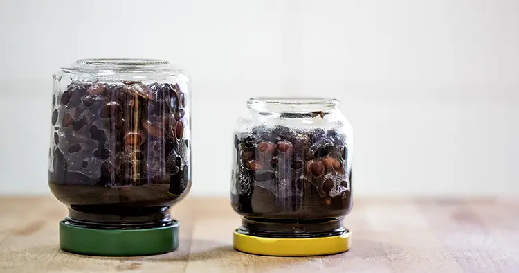 Preserved food in glass jars on wood. Handmade black beans, simmered with sugar and soy sauce.