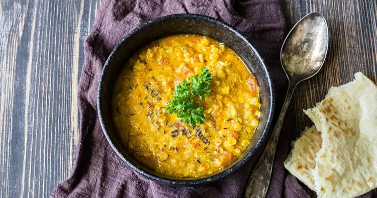 Hot and spicy lentil soup with curly parsley in a black stone bowl on wood background