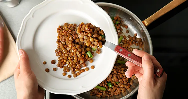 Chef putting tasty lentils onto plate in kitchen
