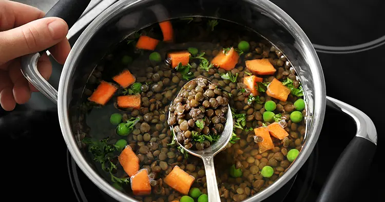 Chef cooking tasty lentils on electric stove in kitchen