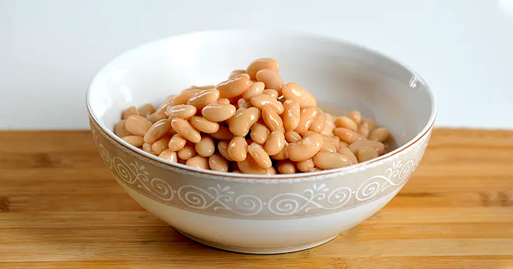 Canned white beans in a deep bowl. Wooden surface. White background. Close-up.