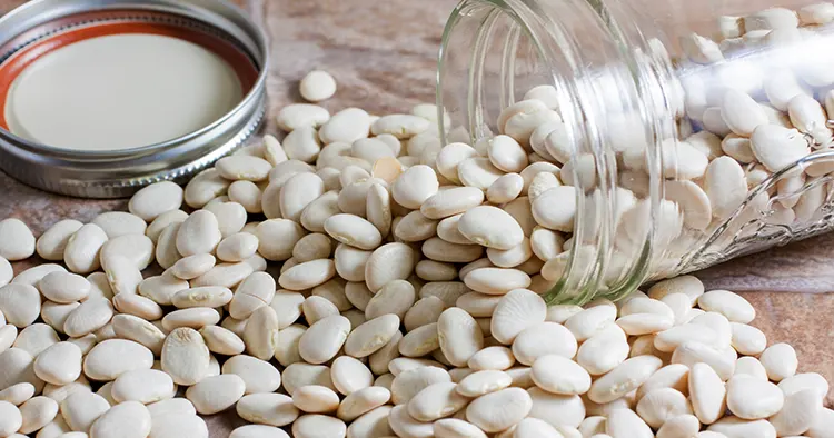 A jar of white lima beans spilled over on a stone counter top.