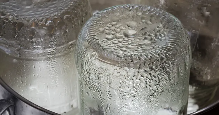 Glass jars in the stainless steel pot during steam sterilization for the home canning, fragment close-up
