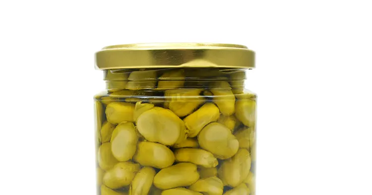 a glass jar with cooked broad beans on a white background