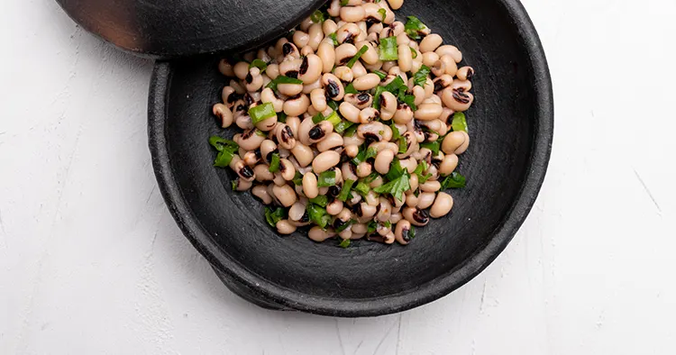 Cooked Fradinho beans salad in a black clay pot, isolated on a white background. Top view.