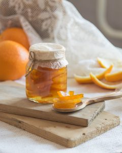 jar of citrus rinds sitting on a wooden board with a spoon of rinds on a wooden spoon